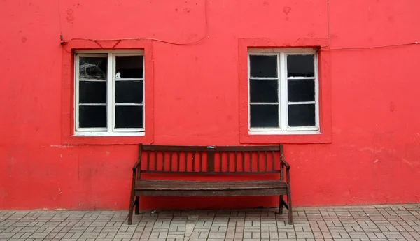 Banco de madeira, duas janelas e parede vermelha — Fotografia de Stock