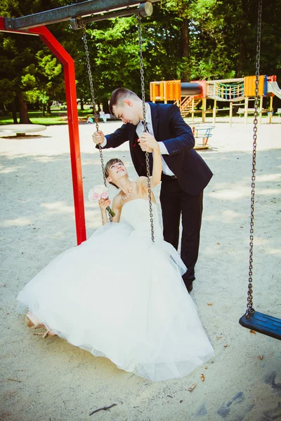 Schönes junges Hochzeitspaar im Park, blonde Braut auf Schaukel — Stockfoto