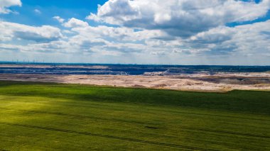 Geleneksel tarım ve rüzgar çiftlikleriyle modern enerji üretimi ile yaz mevsiminde gökyüzünün altındaki termik enerji santrali arasındaki zıtlığı gösteren sanayi manzarası