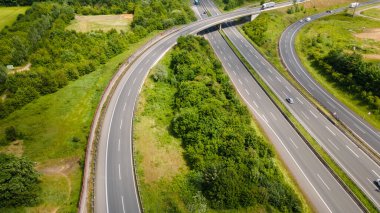 Alman kırsalında güpegündüz yeşil tarlalar ve ormanlarla çevrili karmaşık bir otoyol yonca yaprağı kavşağının insansız hava aracı görüntüsü
