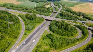 Alman kırsalında güpegündüz yeşil tarlalar ve ormanlarla çevrili karmaşık bir otoyol yonca yaprağı kavşağının insansız hava aracı görüntüsü