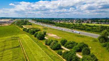 Geleneksel tarım ve rüzgar çiftlikleriyle modern enerji üretimi ile yaz mevsiminde gökyüzünün altındaki termik enerji santrali arasındaki zıtlığı gösteren sanayi manzarası