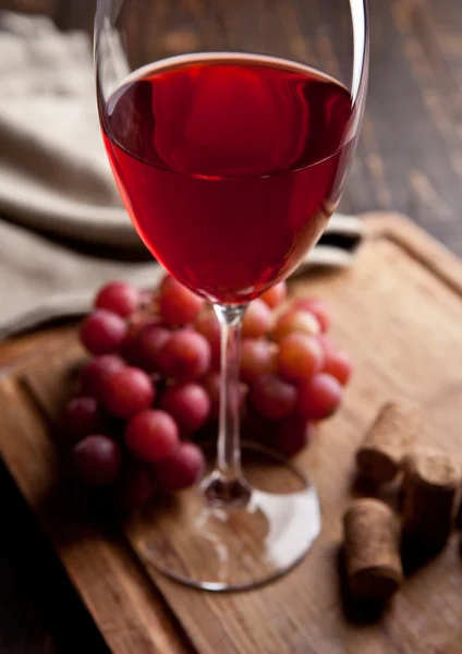 Copo de vinho tinto e uvas em tábua de madeira — Fotografia de Stock