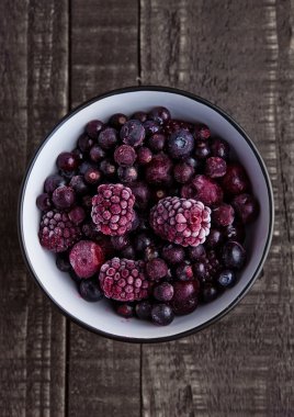 Dondurulmuş çilek ahşap arka plan üzerinde siyah bir kasede karıştırın