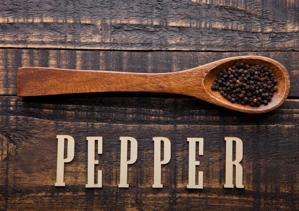 Black pepper on wooden spoon with letters below — Stock Photo, Image