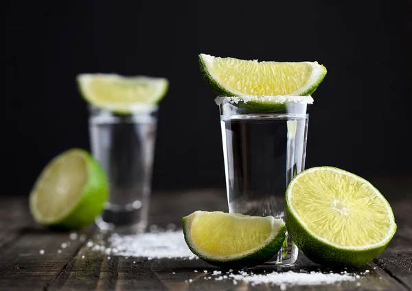 Tequila prata tiros com fatias de limão e sal na tábua de madeira — Fotografia de Stock