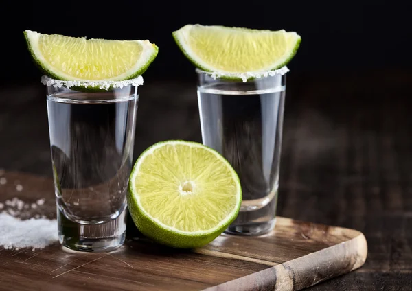 Tequila Silver Shots mit Limettenscheiben und Salz auf Holzbrett — Stockfoto