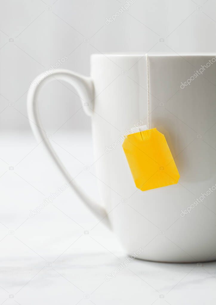 Teabag with yellow blank tag of black tea in white porcelain cup on white background. 