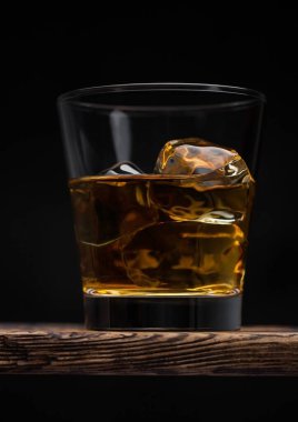 Siyah zemin üzerinde buz küpleri olan bir bardak malt viskisi.