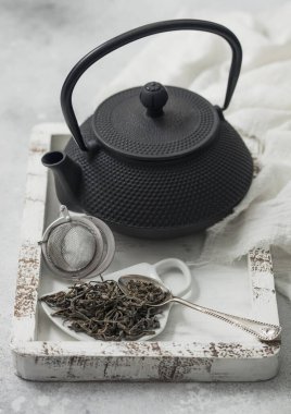 Fincanda yeşil çay, seramik tabakta ve çay topu süzgecinde demir çaydanlık, beyaz tahta kutuda keten kumaşla birlikte.