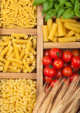 Çeşitli klasik İtalyan makarnası ve kiraz domatesli fesleğen içeren ahşap kutu. Üst görünüm