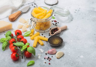 Cam kavanozda makarna. Fesleğenli, sarımsaklı ve yağlı. Arka planda, parmesan ve domatesli..