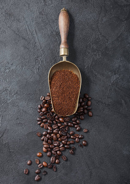Fresh raw organic coffee powder and beans in vintage steel scoop on black background. Top view