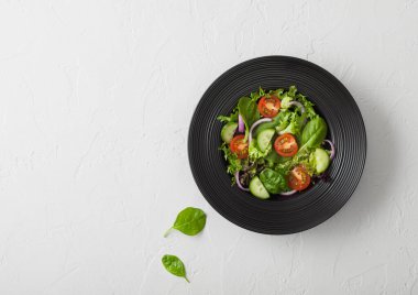 Salatalık ve domates, kırmızı soğan ve ıspanak karışımı taze sebzelerde salata siyah tabak içinde beyaz masa arkasında..