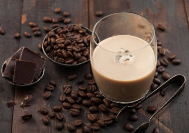 Bir bardak İrlanda kremalı baileys likörü, buz küpleri, kahve çekirdekleri ve koyu ahşap arka planda siyah çikolata. Üst görünüm