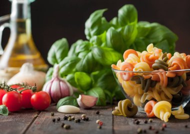 Cam kasede taze çiğ buğday şiş makarna fesleğen, yağ ve biberli domates, ahşap masa arkasında sarımsak ve biber..