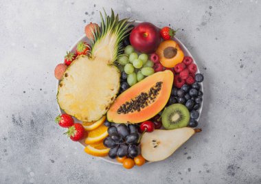 Taze çiğ organik yaz meyveleri ve arka planda beyaz tabakta egzotik meyveler. Ananas, papaya, üzüm, nektarin, portakal, kayısı, kivi, armut, lychees, kiraz ve physalis. Üst görünüm