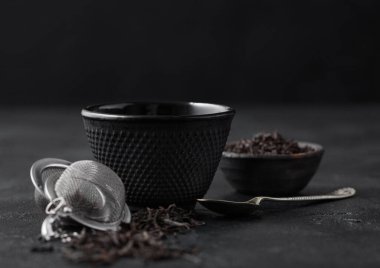 Siyah çay ile demir bardak ve gümüş kaşıkla siyah üzerine gevşek çay yaprağı serpiştirici. Makro