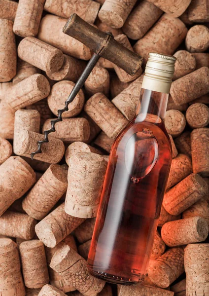 Bottle of pink rose wine and vintage corkscrew on top of various wine corks background.