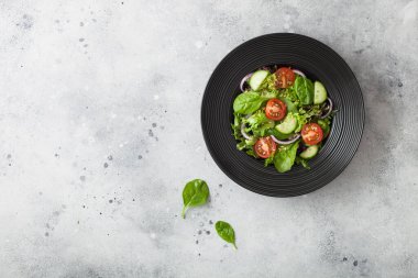 Domatesli, salatalıklı, kırmızı soğanlı ve arka planda siyah kâsede ıspanaklı sağlıklı vejetaryen salatası. Üst görünüm.