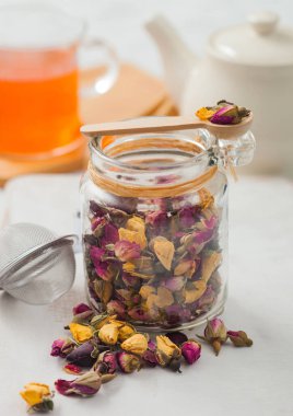 Gül tomurcukları cam kavanozda çayı ahşap kepçe ve süzgeç doldurucuyla karıştırır beyaz zemin üzerinde seramik çaydanlık ve temiz fincanla..