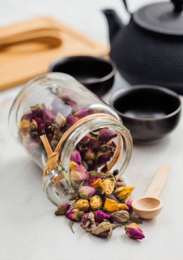 Cam tomurcuk kavanozu çayı beyaz arka planda ahşap kepçeyle siyah demir çaydanlıkla karıştırıyor ve geleneksel çay yapmak için tahta tahtayla karıştırıyor.