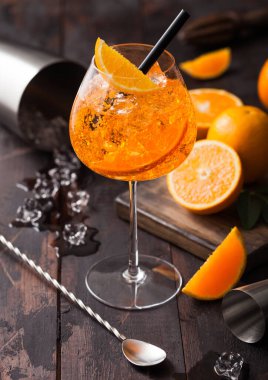 Glass of aperol spritz summer cocktail with oranges and cocktail shaker with bar spoon on wooden background with ice cubes. Top view