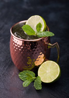 Moscow mule cocktail in a copper mug with lime and mint on dark kitchen table background