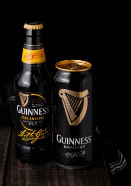 LONDON, İngiltere - 27 Nisan 2018: Koyu ahşap arka planda şişe ve alüminyum bira şişesi. Guinness birası 1759 'dan beri Dublin, İrlanda' da üretiliyor..