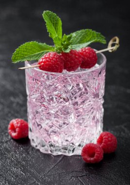 Siyah zemin üzerinde ahududu, nane ve buz küpleri olan bir bardak pembe limonata kokteyli. Metin için boşluk