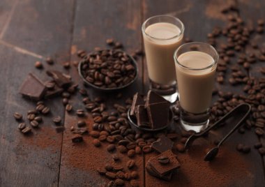 Bir bardak İrlanda kremalı baileys likörü, kahve çekirdekleri ve koyu ahşap arka planda koyu çikolatalı pudra. Makro