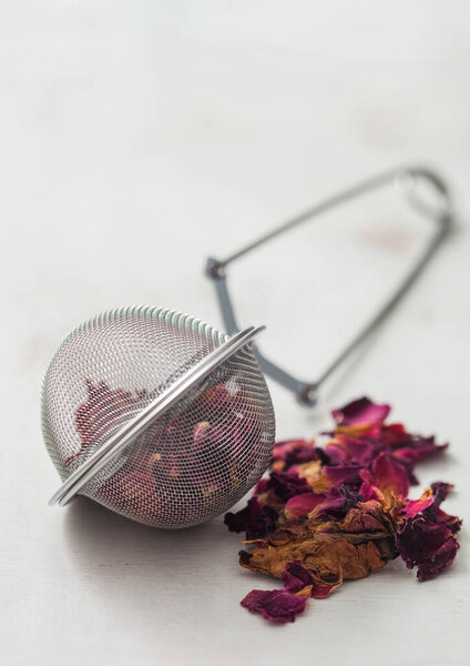 Rose petals craft grade tea with strainer infuser on white background.
