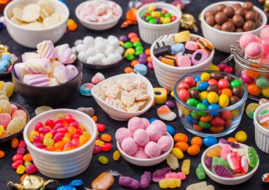 Kavanozda pembe lolipop şekerlemeleri çeşitli sütlü çikolatalar ve jöleli sakızlı şekerler siyah üzerine her çeşit meyankökü ve çilekli şekerler ve çok çeşitli şekerler..