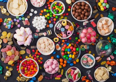 Kavanozda pembe lolipop şekerlemeleri çeşitli sütlü çikolatalar ve jöleli sakızlı şekerler siyah üzerine her çeşit meyankökü ve çilekli şekerler ve çok çeşitli şekerler..
