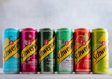 LONDON, İngiltere - 21 Temmuz 2025: Çeşitli Schweppes tonik konserveleri ve arka planda çeşitli aromalı çeşitli aromalar. 