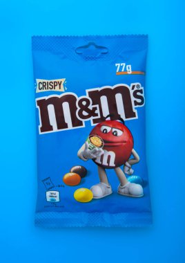 LONDON, UK - 30 HAZİRAN 2025: MM ve M 'nin gevrek sütlü çikolatalı dragee şekerlemeleri mavi üzerine..