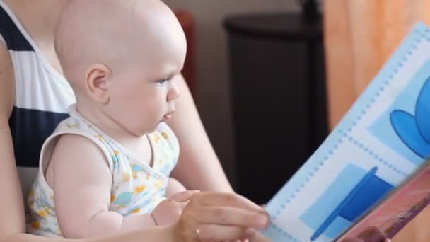 Милый маленький ребенок играет с книгой, сидя с мамой — стоковое видео