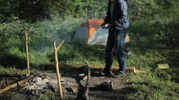 Hombre hablando por teléfono cerca de fogata y tiendas en el bosque — Vídeo de stock