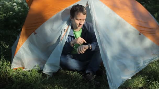 男人打开帐篷，摸摸智能手表，并关闭帐篷 — 图库视频影像