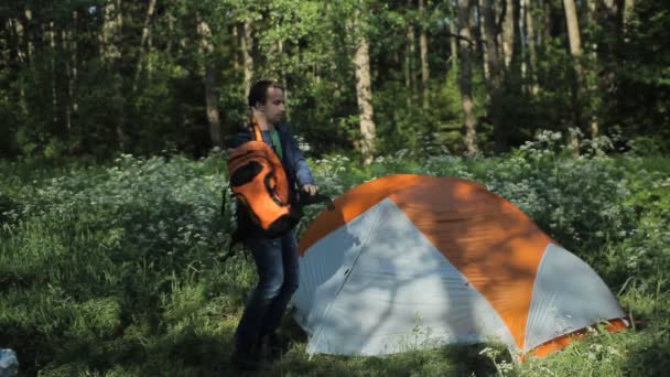 Der Mann trägt einen Rucksack in der Nähe des Zeltes. frühmorgens im Wald — Stockvideo