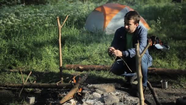 Чоловік кидає дрова на вогонь у кемпінгу. Ранній ранок у лісі — стокове відео