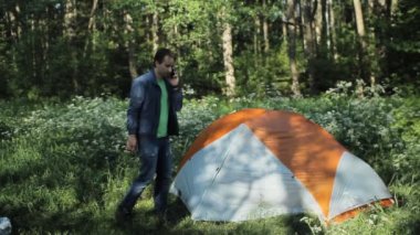 Çadırın yanındaki telefonla arayan bir adam. Ormanda sabahın erken saatlerinde