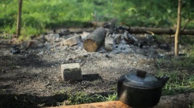 Telefon sigara yangınının yanında bir taşa konmuştur. Ön planda, kamp su ısıtıcısı. Ormanda sabahın erken saatlerinde