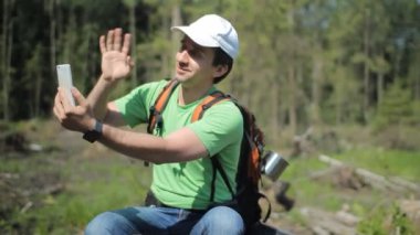 Bir adam bir sırt çantası ile bir ağaç eski bir güdük üzerinde oturuyor. Telefonda tıklama