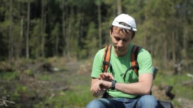 Bir sırt çantası ile erkek turist smartwatch dokunur. Bir yaz günü orman arka planı