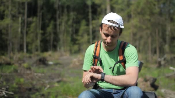 Male tourist with a backpack touches smartwatch. Against the background of a summer day forest — Stock Video