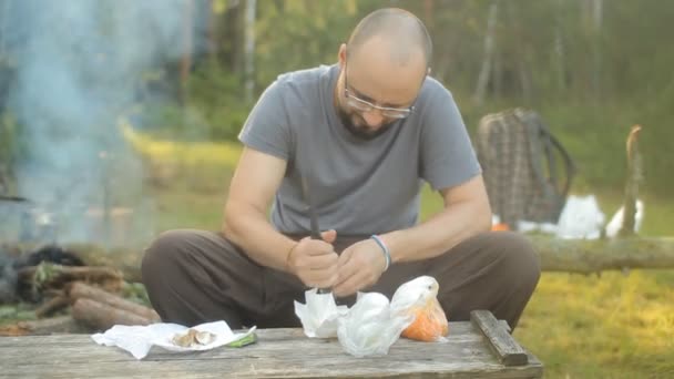 Az ember egy késsel őrölni száraz leves egy kirándulás. Közelében a tűz füst távozik — Stock videók