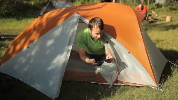 L'homme fait toucher tablette hors de la tente. Ouvrez la tente, touchez l'écran des tablettes et fermez la tente. Journée ensoleillée dans la forêt — Video