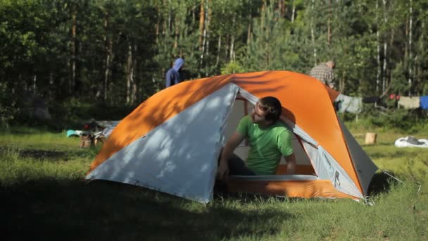 Mannen bär skor och går ur tältet i lägret. Solig dag i skogen — Stockvideo