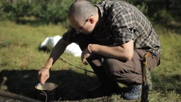 L'uomo mescola il porridge nel piatto. Vicino al fuoco emette fumo — Video Stock